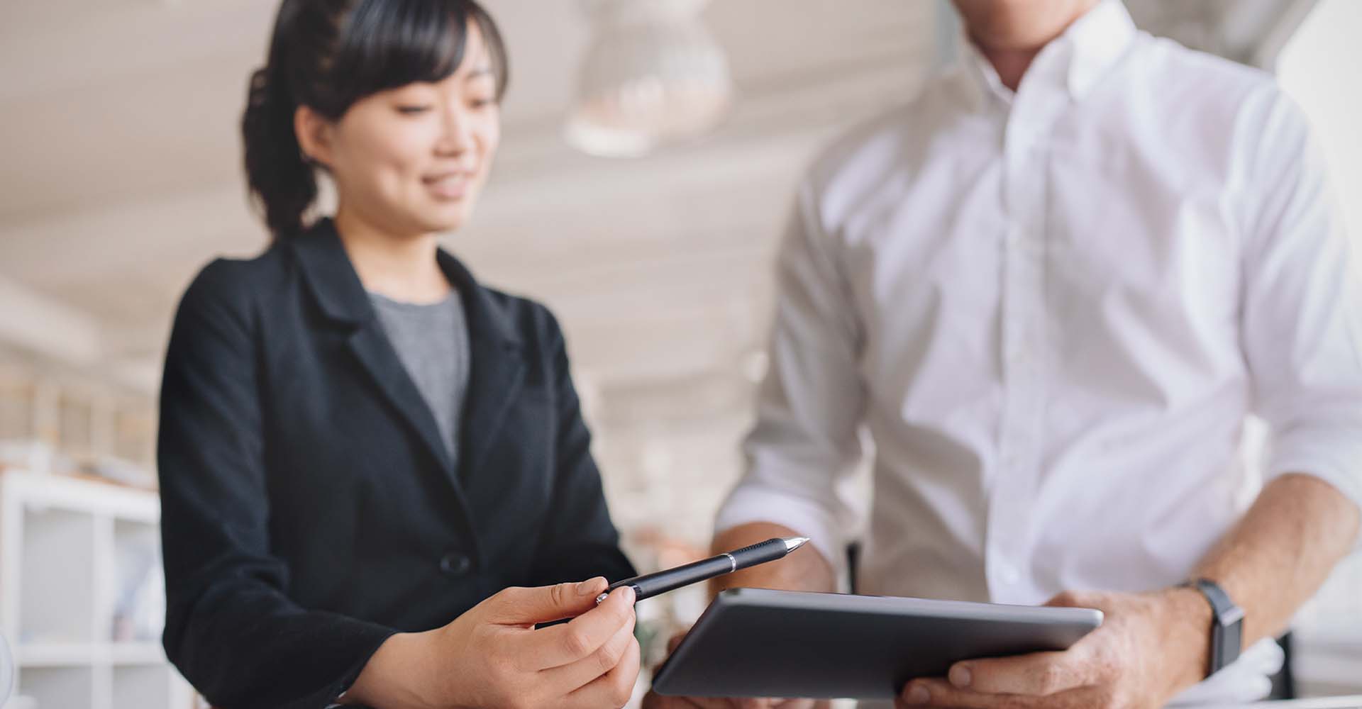 Two professionals discussing work over a tablet in an office.