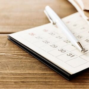 A calendar planner with a pen on a wooden table.