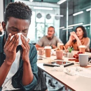 A man sneezing into a tissue in a meeting room.