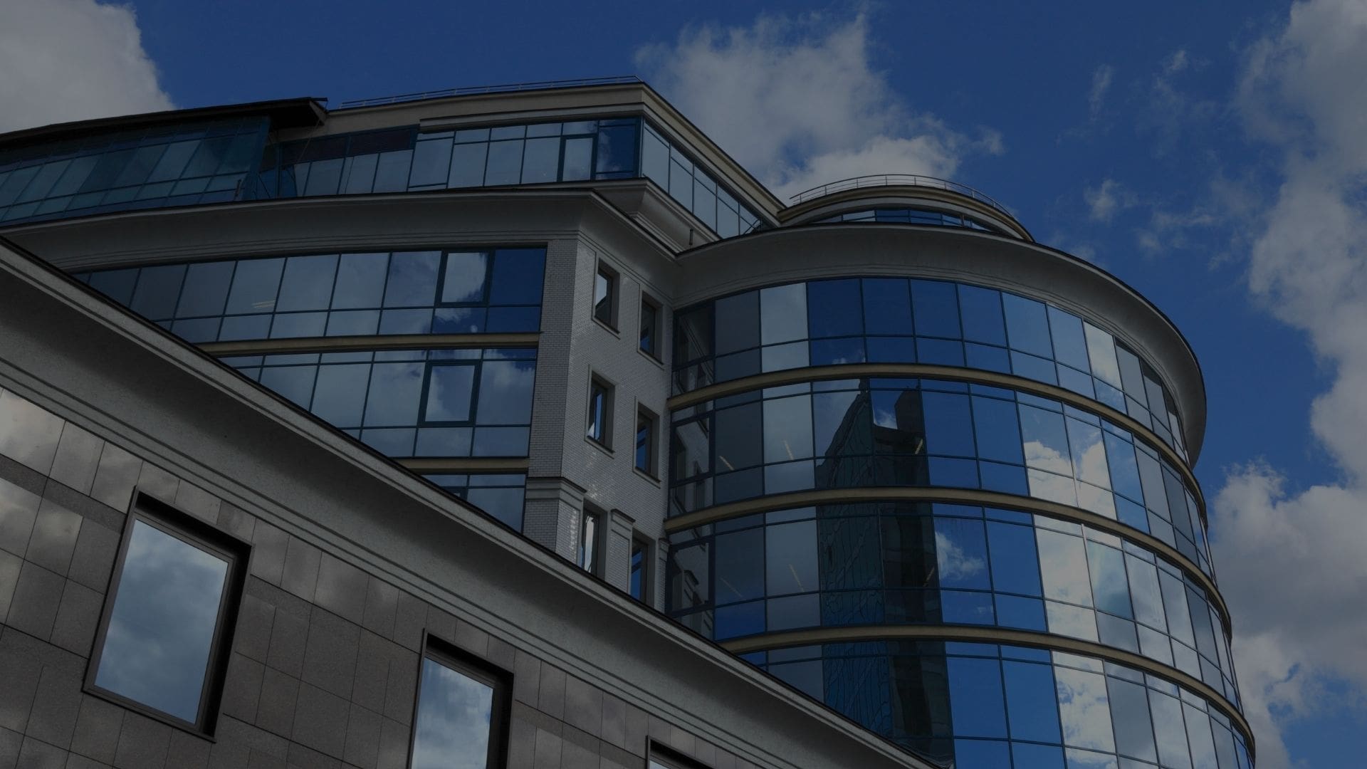 Modern glass and concrete building under a blue sky with clouds.