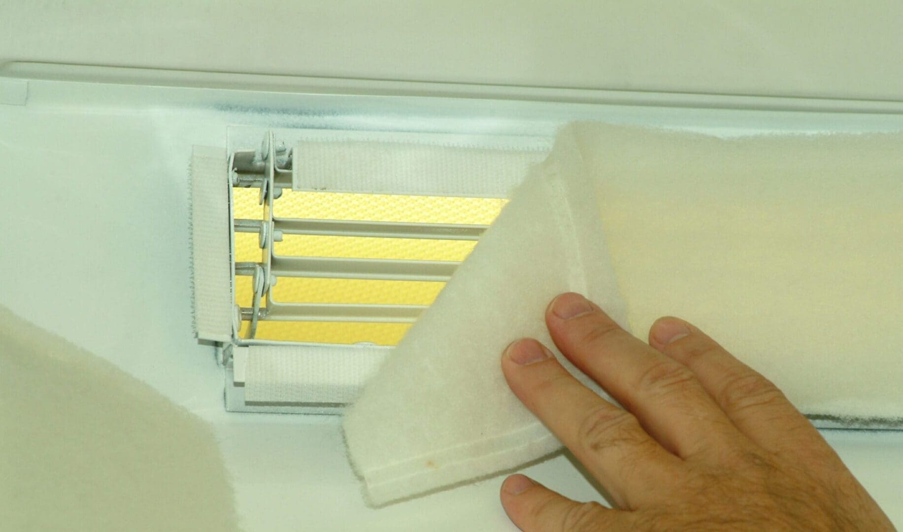 A hand adjusts the Comfort First Filtered Diffuser's fabric cover, uncovering a yellow grid pattern beneath the metal grilles.