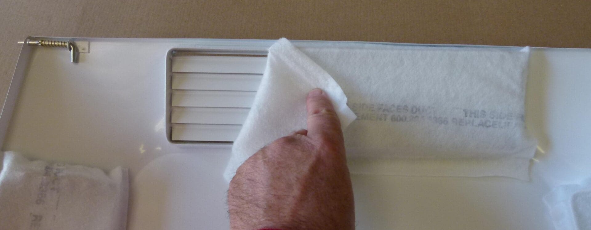 A hand inserts a filter from the Filter Subscription Program for Comfort First Filtered Diffuser into a vent on a white appliance.