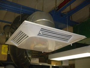 The Comfort First Filtered Diffuser is a ceiling-mounted, commercial, 4-way adjustable vent diverter with rectangular slats for filtered air distribution via ducts, surrounded by various pipes and fixtures.