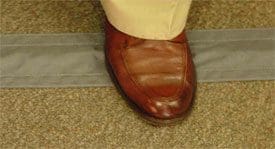 A brown leather shoe steps on a Safcord on a carpeted floor.